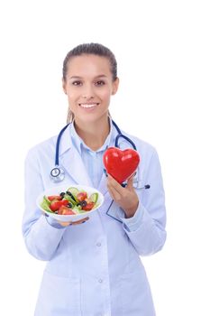 Portrait of a beautiful woman doctor holding a plate with fresh vegetables and red heart. Woman doctors