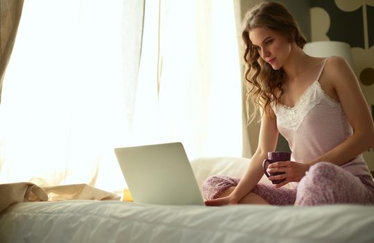 Young beautiful woman sitting in bed with laptop.