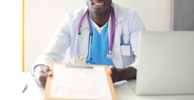 Portrait of young male doctor wearing headset while using computer at desk in clinic. Doctor