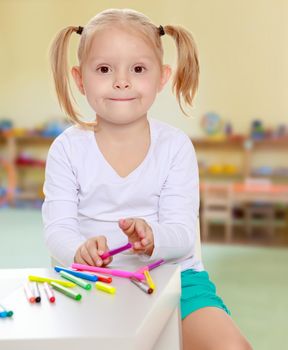 The concept of pre-school education of the child among their peers . on the background of the playroom with shelves for toys. Montessori.Pretty little blonde girl drawing with markers