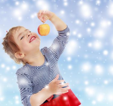 Nice little blonde girl with a red bow on the head holding the tail in front of the face of a delicious Apple . close-up.Gentle blue Christmas background with white snowflakes abstract.