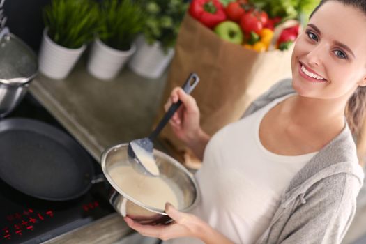 Young woman prepares pancakes in the kitchen while standing near the table. Woman in the kitchen. Cooking at kitchen