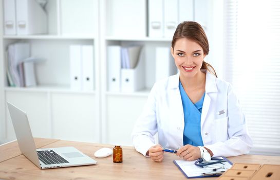 Beautiful young smiling female doctor sitting at the desk