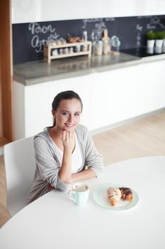 Woman drinking tea with sweet croissant at the kitchen table