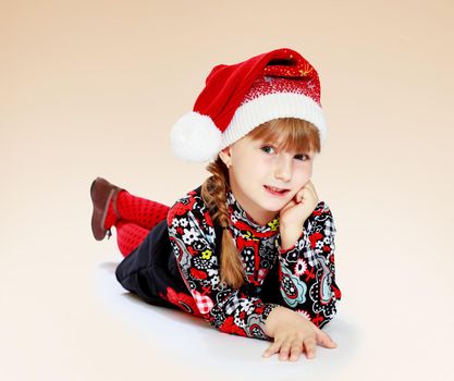 Positive little girl in a cap of Santa Claus is on the floor.