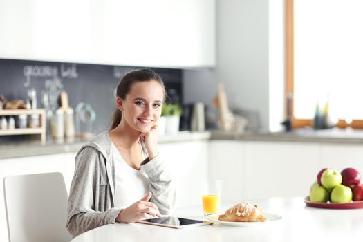 Young woman with orange juice and tablet in kitchen
