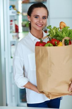 Young woman holding grocery shopping bag with vegetables .Standing in the kitchen.