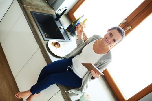 Beautiful young woman using a digital tablet in the kitchen.