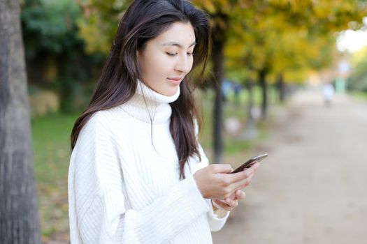 Korean girl typing by smartphone and walking in park. Concept of asian female person and chinese modern technology.