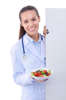 Portrait of a beautiful woman doctor holding a plate with fresh vegetables standing near blank. Woman doctors.