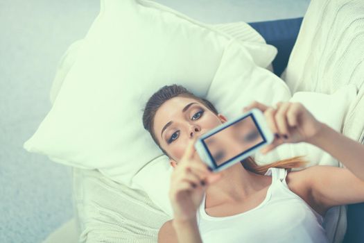 Happy woman taking a photo of herself with her mobile phone in a bedroom