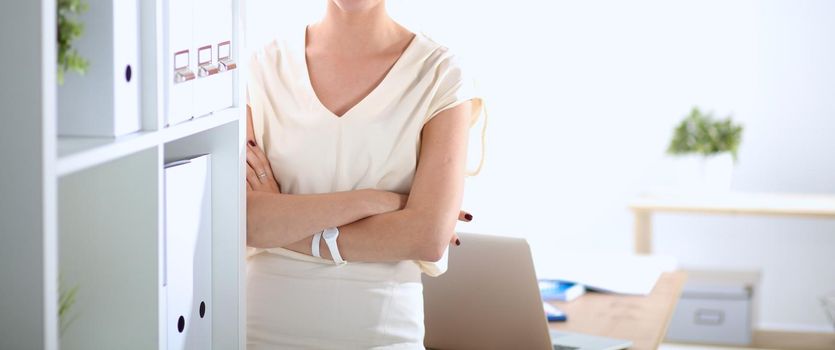 Attractive businesswoman standing near wall in office .