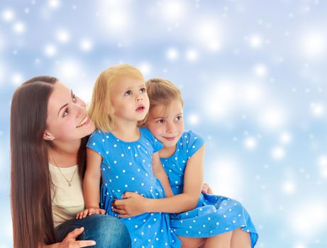 Beautiful young mother with her two daughters. All look up.On a blue background with large, white, Christmas or new year's snowflakes.