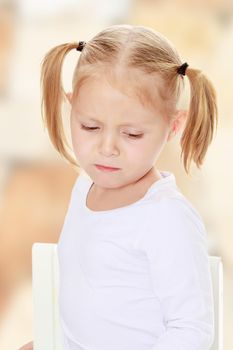 Beautiful little blonde girl with pigtails on his head, white t-shirts without a pattern. The girl is upset about something. Close-up.