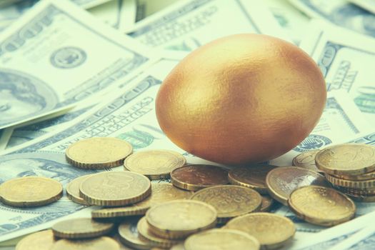A gold egg lying on dollars and coins