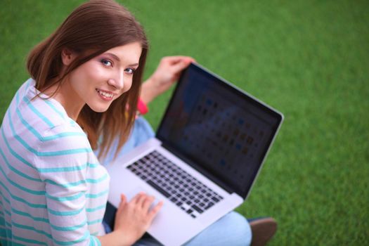 Young woman with laptop sitting on green grass.