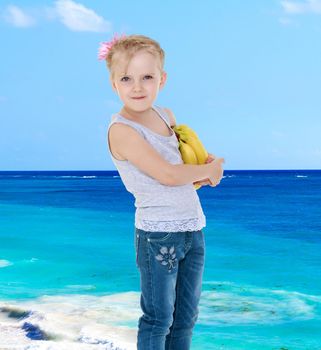 Smiling little girl with bananas in hand on a background of the sea.