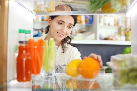 Portrait of female standing near open fridge full of healthy food, vegetables and fruits. Portrait of female.
