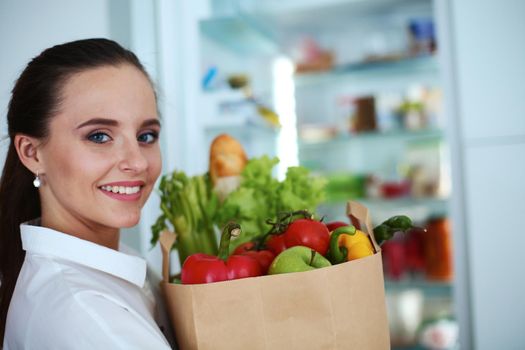 Young woman holding grocery shopping bag with vegetables .Standing in the kitchen.