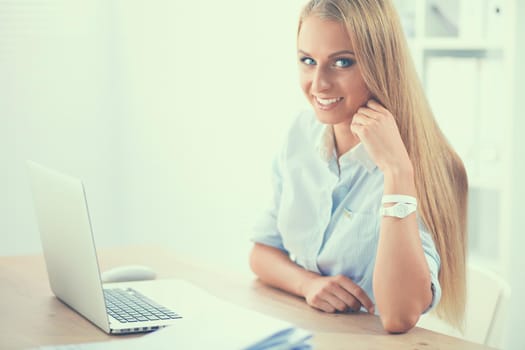 Attractive businesswoman sitting on a desk with laptop in the office.