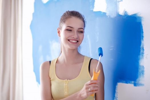 Beautiful young woman doing wall painting, standing .