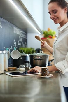 Young woman standing by the stove in the kitchen .