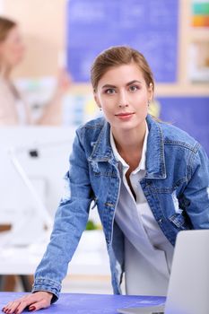 Two young woman standing near desk with instruments, plan and laptop