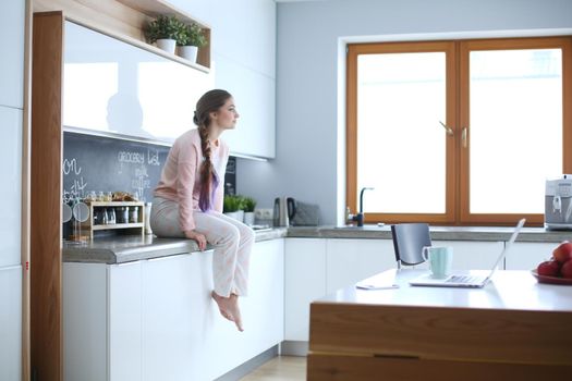 Young woman sitting on table in the kitchen