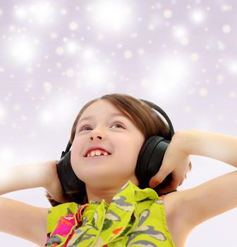 Blue Christmas festive background with white snowflakes.Closeup portrait of little girl listening to music through big black headphones.