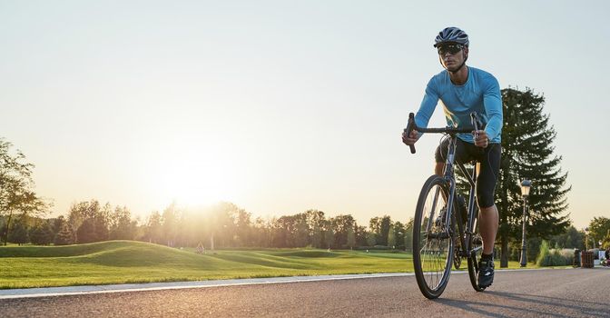 Rear view of athletic man in sportswear standing with bicycle on the road. Riding mountain road bike on a sunny summer day. Healthy active lifestyle and sport concept