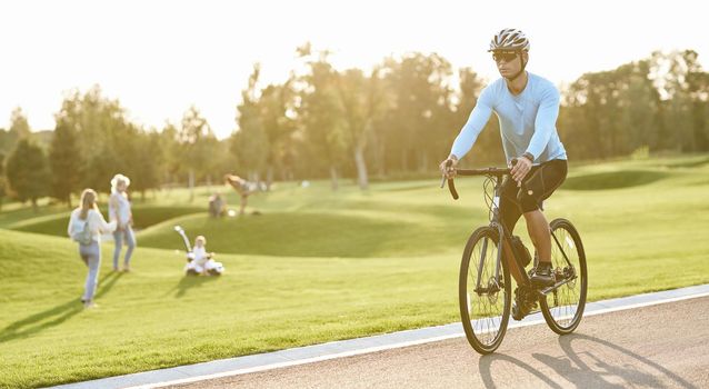 Active lifestyle. Young athletic man in sportswear and protective helmet riding mountain bike in park during sunset, cycling outdoors on a summer day