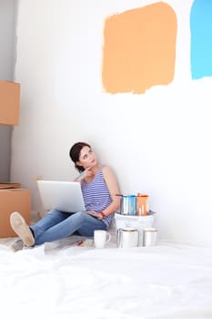 Young woman portrait while painting new apartment ,sitting with laptop. Young woman with laptop.