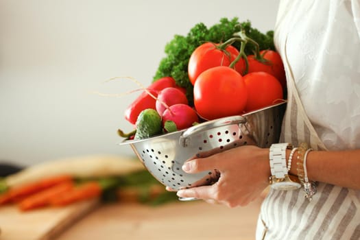 Young woman holding vegetables standing in kitchen .