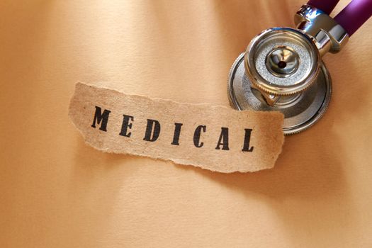 A word medical written on a ripped piece of paper and stethoscope