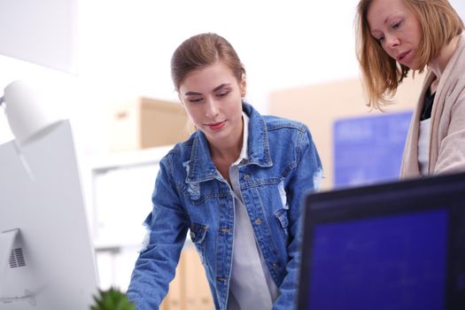 Two young woman standing near desk with instruments, plan and laptop