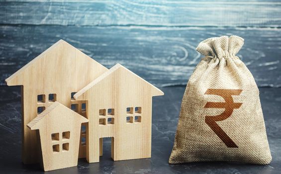 Indian rupee money bag and figurines of residential buildings. Property tax. Municipal budgeting. Financing urban development and infrastructure projects. Increase in investment attractiveness