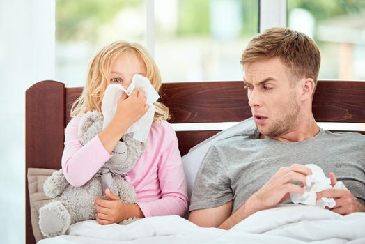 Young father and daughter suffering from flu or cold, having runny noses while resting in bed together at home. Virus disease. Coronavirus concept. Sick family at home. Health concept