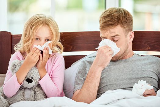 Young father and his daughter are suffering from flu or cold and runny nose while lying in bed together at home. Virus disease. Coronavirus concept. Sick family at home. Health concept