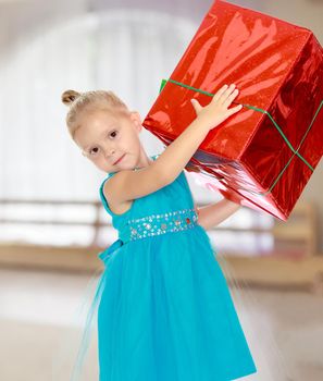 Caucasian little girl in a blue dress, holding the hands of the big red box that is a gift.The girl lifted the box over his head.