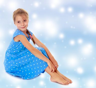 Beautiful little girl dressed in blue polka-dot dress , sitting barefoot.On a blue background with large, white, Christmas or new year's snowflakes.