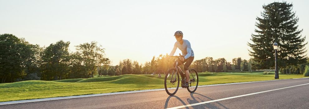 Rear view of athletic man in sportswear standing with bicycle on the road. Riding mountain road bike on a sunny summer day. Healthy active lifestyle and sport concept