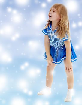 On a blue background with white blurry circles, like Christmas snowflakes. Cute little unkempt girl in a short blue dress. Girl looking to the side with his hands on his knees.