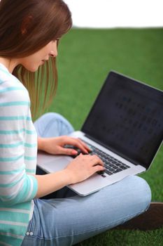 Young woman with laptop sitting on green grass.