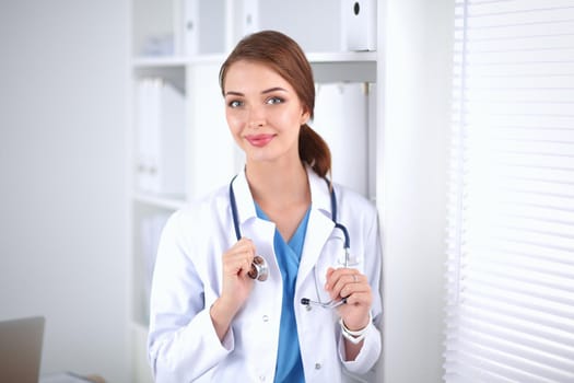 Woman doctor is standing near window with crossed arms,isolated