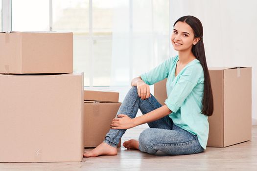 Young entrepreneur, SME, freelance woman working online, business by using smartphone, making purchase, order and preparing packages. Woman sitting near stack of boxes and looking at the camera with a smile. Concept of success