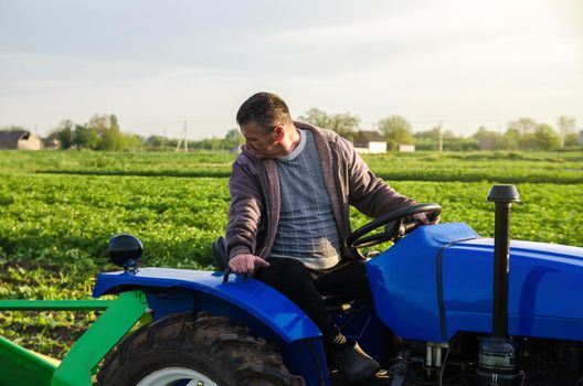 A farmer on a tractor monitors the operation of equipment for harvesting potatoes. Farming and farmland. Simplify speed up work with technology and machines. Agro industry and agribusiness