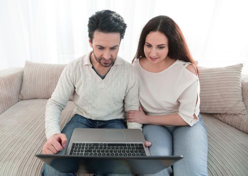 married couple sitting on the couch and looking at the laptop screen.the concept of joint interests