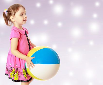 Beautiful little girl in a pink dress throwing a big striped ball. Turned sideways. Close-up.On new year's or Christmas purple background where glowing large white star.