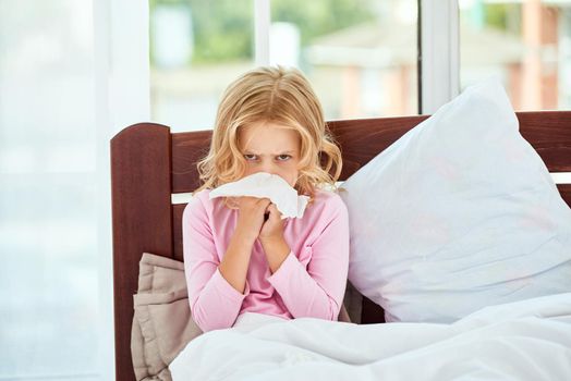 Little girl with runny nose suffering from cold or flu while lying in bed at home. Virus disease. Coronavirus concept. Healthcare concept