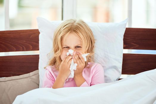 Portrait of sick little girl with runny nose suffering from cold or flu while lying in bed at home. Virus disease. Coronavirus concept. Healthcare concept